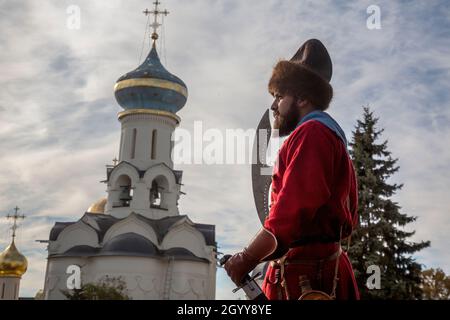 Sergiyev Posad, Russia. 9th October, 2021 A man dressed in a Streltsy costume walks against the background of orthodox christianity church at the Trinity Lavra of St. Sergius in Sergiyev Posad ancient russian town near Moscow, Russia. Streltsy were the units of Russian firearm infantry from the 16th to the early 18th centuries and also a social stratum Stock Photo