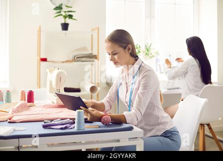 Woman who works as dressmaker using tablet while sitting at table in her atelier Stock Photo