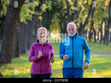 Senior couple jogging in park on sunny autumn day Stock Photo
