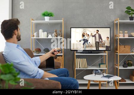 Relaxed young man sitting on couch in living room and watching movie on television Stock Photo