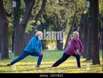 Senior couple stretching legs and warming up for exercise and jogging in park on sunny autumn day Stock Photo