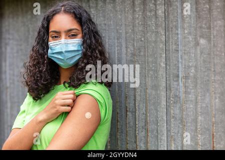 Vaccinated girl teenager teen mixed race biracial African American female young woman wearing face mask in Coronavirus COVID-19 pandemic showing vacci Stock Photo