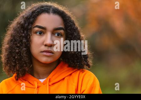 Outdoor portrait of beautiful sad thoughtful depressed mixed race biracial African American girl teenager female young woman outside wearing an orange Stock Photo