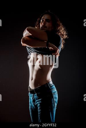 Studio fashion portrait of a hipster man while taking off his t-shirt Stock Photo