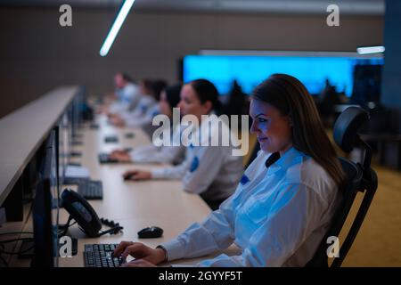 Group of Security data center operators (administrators) working in a group at a CCTV monitoring room while looking at multiple monitors ( computer sc Stock Photo