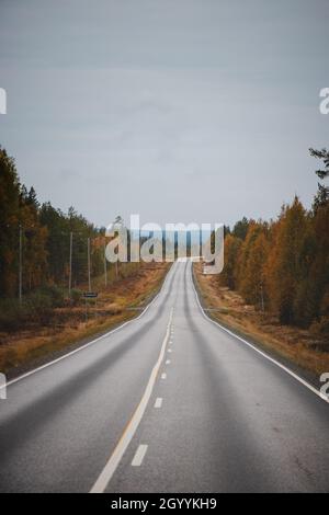 Road trip in the Kainuu region of Finland in autumn. Beautiful asphalt road surrounded by many leafy red-orange trees. Stock Photo