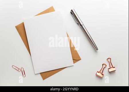 Greeting, wedding or congratulations stationery mockup. Blank sheet of paper, craft envelope, fountain pen and various paper clips on clean white desk Stock Photo