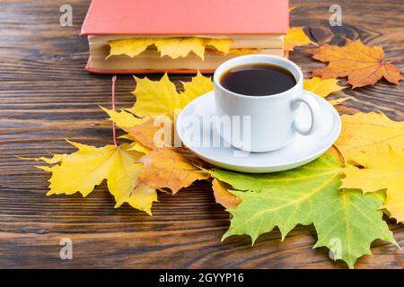 coffe cup on wooden table with book colorful autumnal maple leaves. Stock Photo