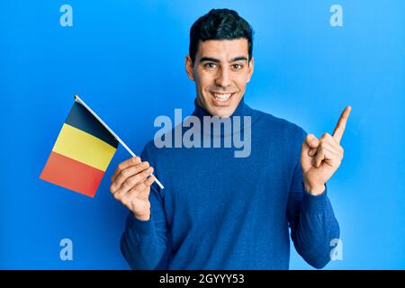 Handsome hispanic man holding belgium flag smiling happy pointing with hand and finger to the side Stock Photo