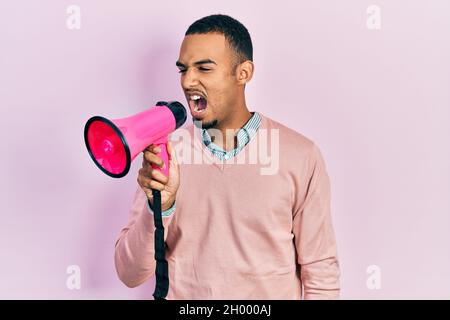 Young african american man shouthing and screaming through megaphone over pink isolated background Stock Photo