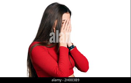 Young brunette teenager wearing red turtleneck sweater with sad expression covering face with hands while crying. depression concept. Stock Photo