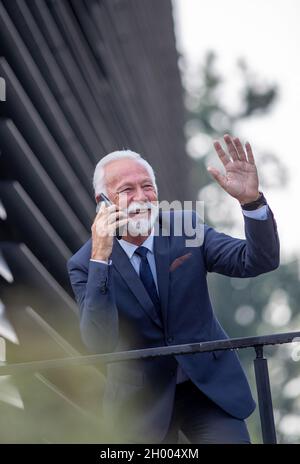 Smiling mature adult businessman standing on balcony of office building, talking on mobile phone and waving hand Stock Photo