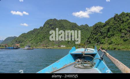 Looking at the blue river and high mountain from the bow of a small wooden boat in Phong Nha - Ke Bang National Park, Quang Binh Province, Vietnam Stock Photo