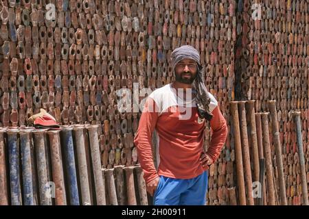 Young handsome middle eastern migrant laborer wearing muslim male headdress, working for scrap metal supply warehouse for recycling  Stock Photo