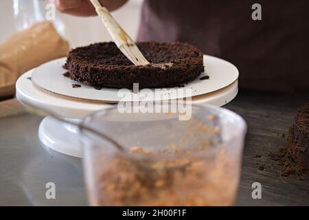 Woman pastry chef impregnates chocolate sponge cake on stand, close-up. Cake making process, Selective focus Stock Photo
