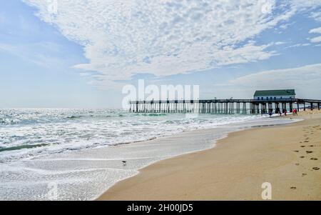 A seascape view of a wooden fishing pier extending into the foamy waves of the Atlantic Ocean. Kitty Hawk, Outer Banks, North Carolina. Copy space. Stock Photo