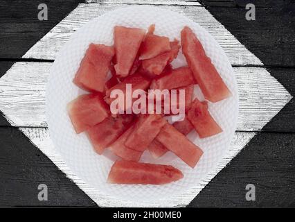 A top view shot of seedless watermelon chunks in white porcelain plate on a black and white painted wooden background Stock Photo