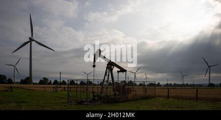 Old rusty oil hauling machines in front of modern wind turbines symbolizing energy transition at the face of climate change Stock Photo