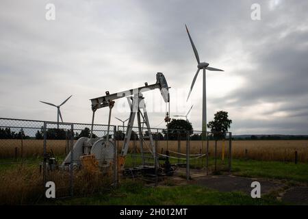 Old rusty oil hauling machines in front of modern wind turbines symbolizing energy transition at the face of climate change Stock Photo