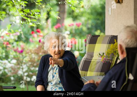 Senior man and woman talking on terrace with beautiful floral garden in background Stock Photo