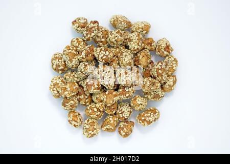 Roasted peanuts in sugar with sesame seeds on a white plate top view. Peanuts in honey caramel and sprinkled with sesame seeds. Sweet snacks with nuts Stock Photo
