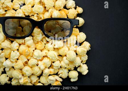Popcorn and glasses for watching movies in 3d format on a black background. Cinema theme, background with place for text. Face with glasses made of po Stock Photo