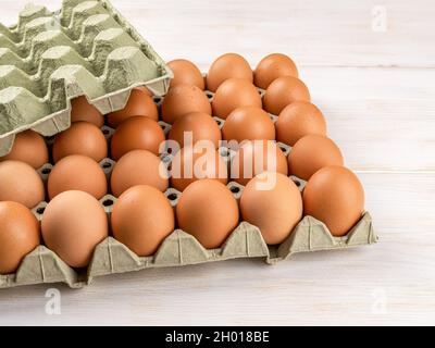 Brown chicken eggs in the cardboard tray on a white wooden table. Thirty raw organic hen eggs with brown shell in the biodegradable carton container. Stock Photo