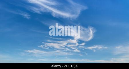 Wispy cirrus clouds high in the blue sky. Uncinus and fibratus subforms of cirrus clouds on a sunny day. Clouds classification, meteorology, weather. Stock Photo