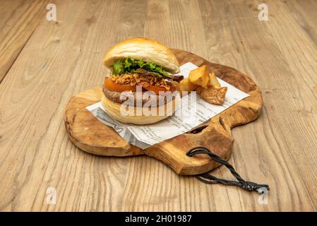 Vegan Beef Burger with Tomato Slices, Crispy Fried Onions, Lettuce and Garnish of Chopped Roasted Potatoes Stock Photo