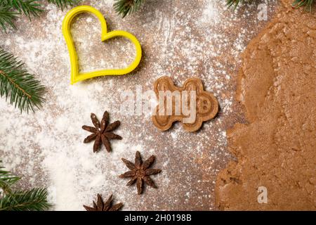Christmas is on the way! Gingerbread man cookie, star anise fruits, heart-shaped cookie cutter, fir branches, a piece of rolled out gingerbread dough. Stock Photo