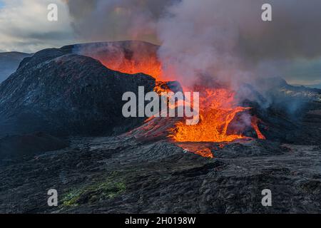 Daytime volcanic eruption on Reykjanes peninsula. Side view of the crater opening with flowing lava. Crater from Fagradalsfjall volcano in Iceland in Stock Photo