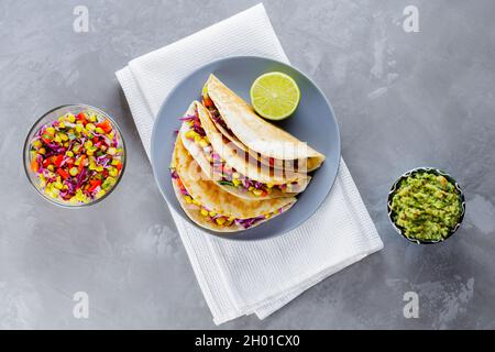 Mexican tacos with vegetables and guacamole on gray background. Vegan tacos with corn, purple cabbage and tomatoes on a gray plate. Copy space. Top vi Stock Photo