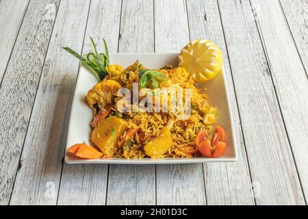 Indian recipe tray of biryani rice with vegetables. Cauliflower and boiled potatoes, carrots and peppers with lemon and cherry tomatoes Stock Photo