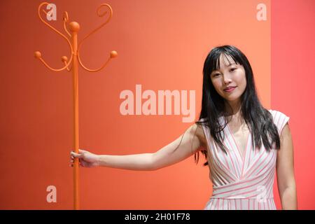 Young asian woman pose with a red orange monochrome coat rack. Studio shot. Stock Photo