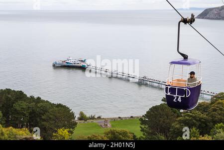 A tourist on the cable car going up the Great Orme summit leaving Llandudno and its pier in the background.  Seen in October 2021 on the North Wales c Stock Photo