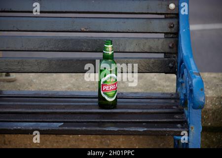 Empty glass bottle seen left behind on a seat outdoors. Stock Photo