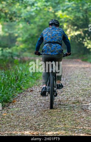 older man riding a mountain bike or cycling through an autumn woodland along a track or trail on the isle of wight uk. mountain bike rider in woods. Stock Photo