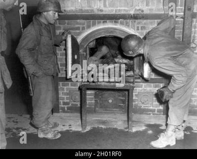 Three U.S. soldiers look at bodies stuffed into an oven in a crematorium in April of 1945. Dachau concentration camp. Stock Photo
