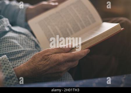 Close up of senior's hands holding book. Old man reading at home Stock Photo