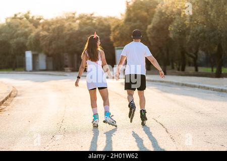 Couple in their backs skating while holding hands in an urban park Stock Photo