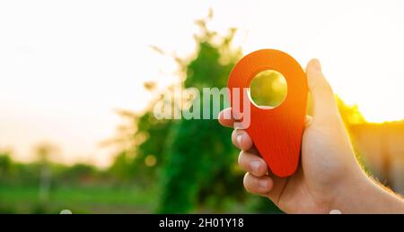 A hand is holding a red location marker in the sunset background. Navigation and exploration. The concept of tourism and travel. Destination. Holiday, Stock Photo