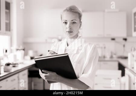 Portrait of young, confident female health care professional taking notes during inventory in scientific laboratory or medical doctors office Stock Photo