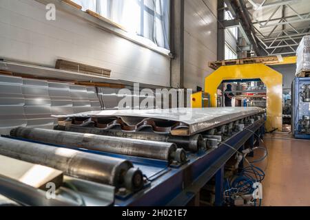 Conveyor with finished packaged products of metal tile sheets for roof in metalworking factory workshop. Stock Photo