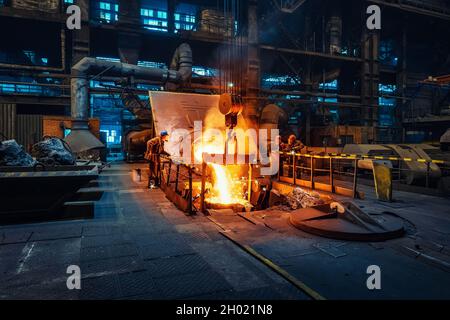 Metal cast process in blast furnace in metallurgical plant or factory. Liquid iron molten metal pouring in container, heavy industry background. Stock Photo