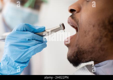 Dental Treatment. Dentist Woman Using Dental Drill For Black Male Patient In Clinic, Young African American Man Sitting With Opened Mouth, Enjoying Pr Stock Photo