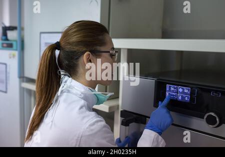 Woman biologist working on touch screen of incubator display, adjusting conditions in laboratory Stock Photo