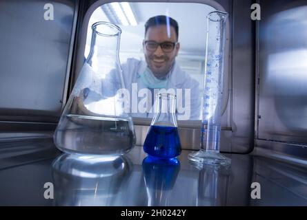 Biologist looking through glass door into incubator with samples and chemicals in laboratory. Shoot from inside Stock Photo