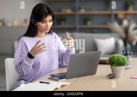 Portrait of focused woman in headphones looking at laptop screen and talking during webinar, consulting client, explaining lesson or business strategy Stock Photo