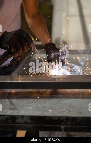 details of a person's hand wearing protective gloves while using a metal welding tool, sparks from the machine, manual work Stock Photo