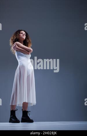 Beautiful girl with curly hair. Ballerina in white dress and black boots. Stock Photo